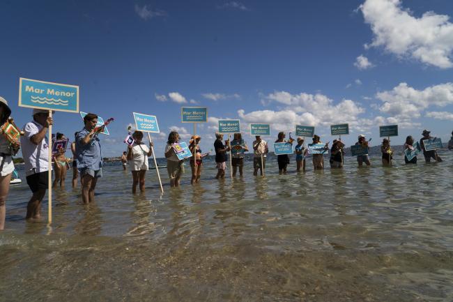 A large group of people standing in the sea holding signs.