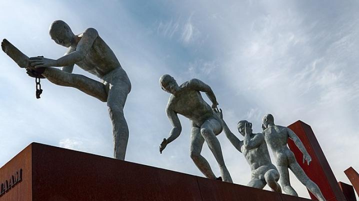 a sculpture in bronze of four people breaking free of their chains