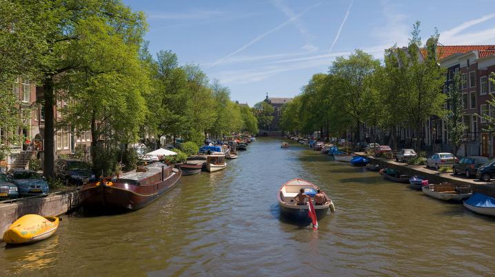 A small boat passes through an Amsterdam canal on a sunny day