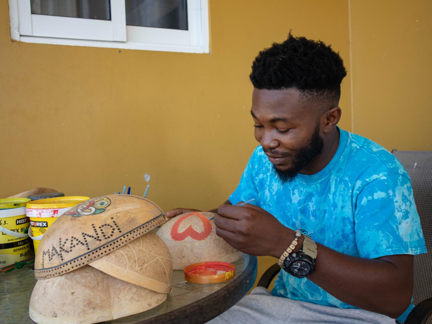 Artist Winston Vola painting a gourd bag. The sweater he is wearing is his latest design from the Makandi brand.