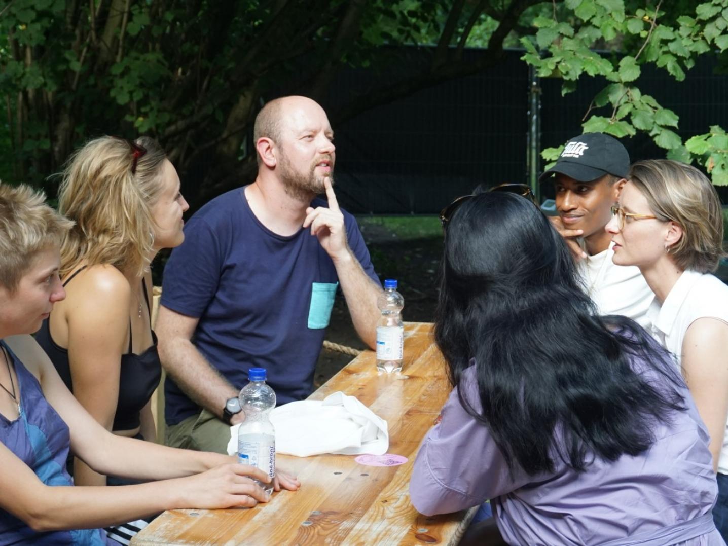 Six people sitting outside around a table talking