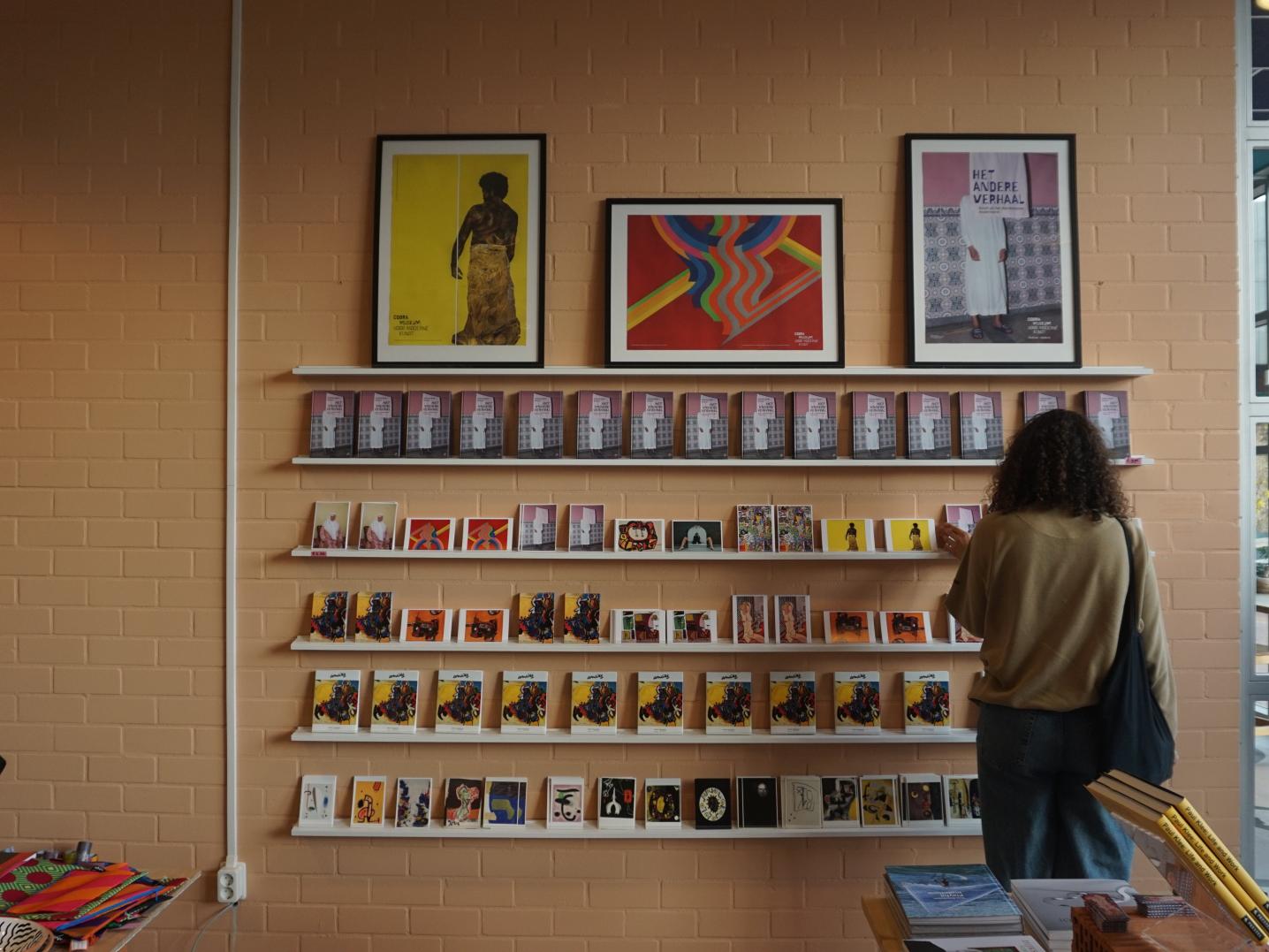 a woman looking at a rack filled with postcards and posters of artists' work