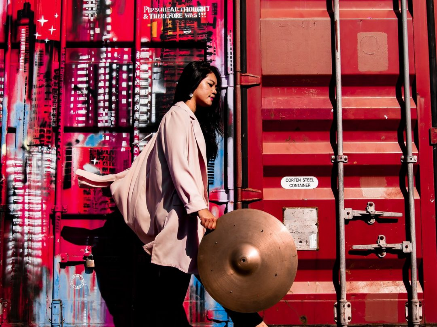 Girl holding cymbal in front of shipping containers