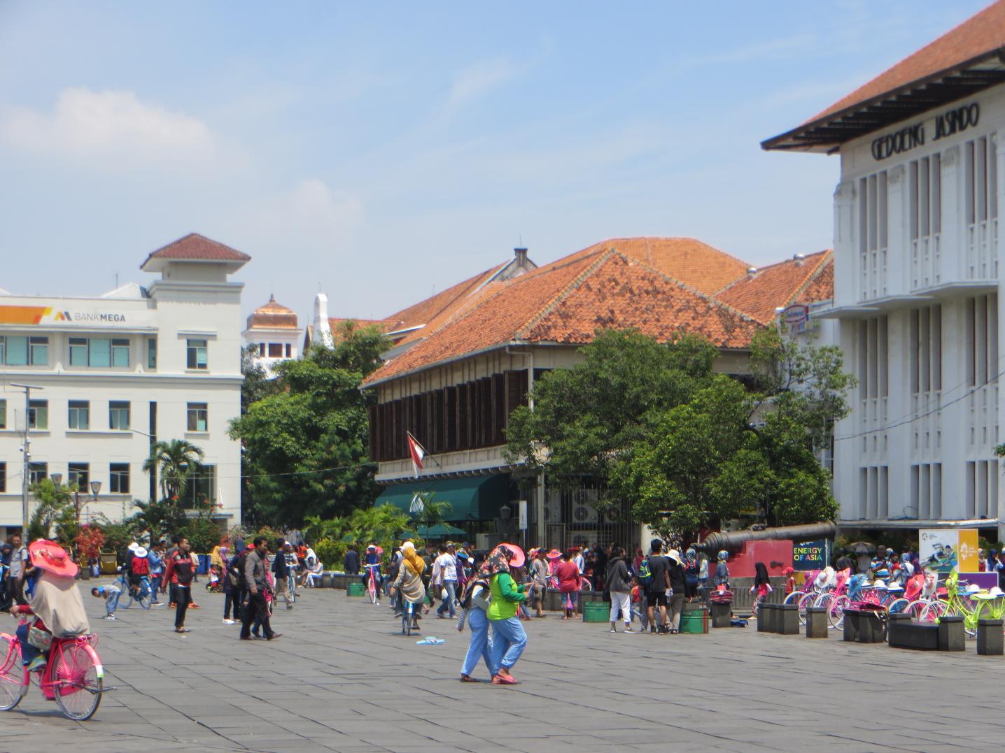 a 2018 photo of Fatahillah Square in Kota Tua, the historical inner city of Jakarta, which shows colonial buildings and many people hanging out and walking around