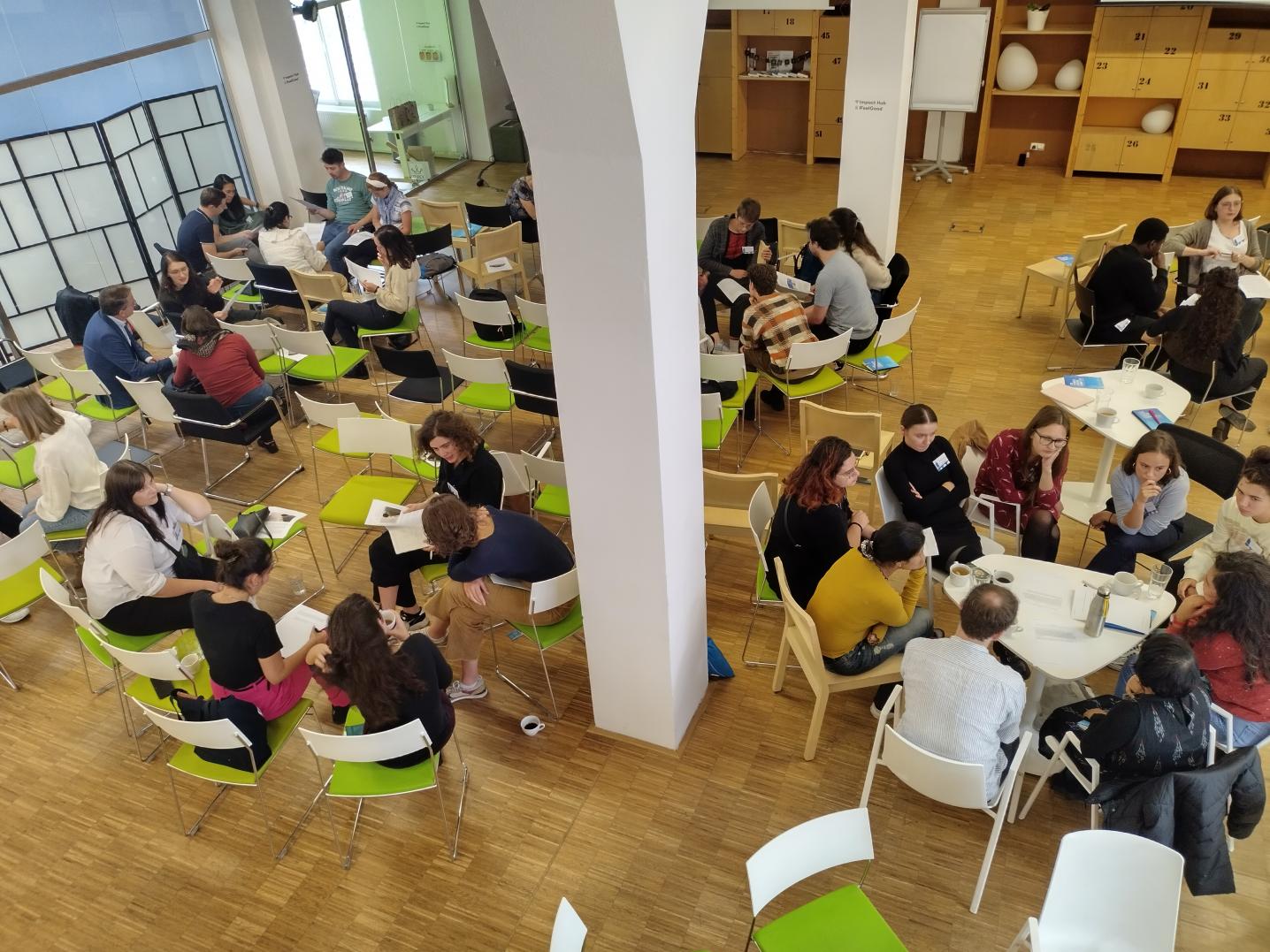 Overview of room full of chairs, people in small groups