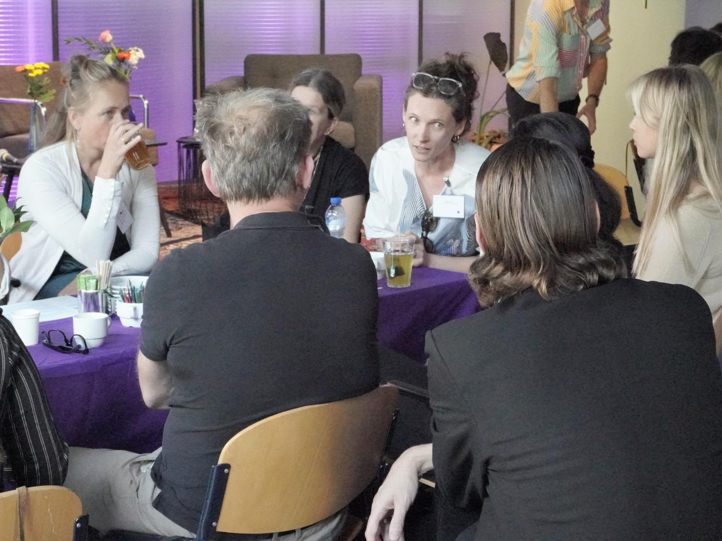 Group of people sitting in a purple lit room talking with each other