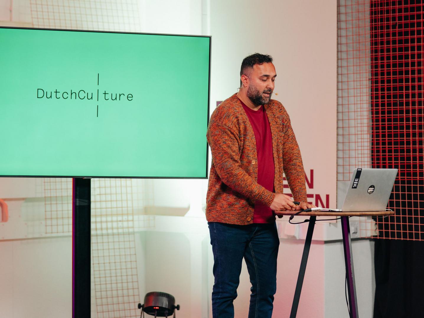 A man talking on a stage with the logo of DutchCulture behind him