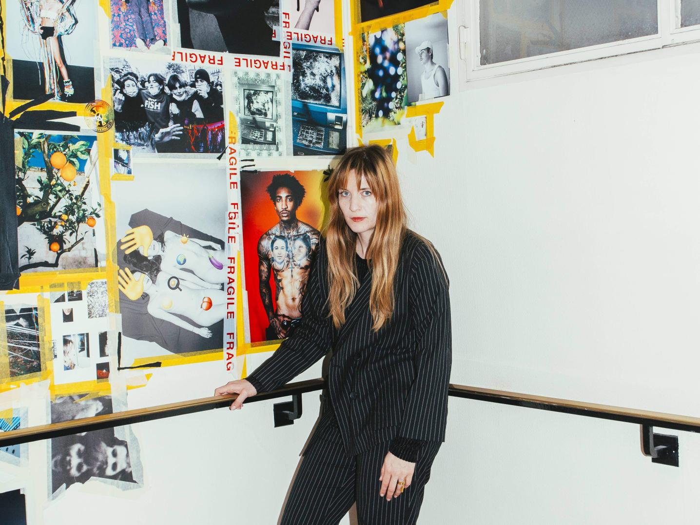 Artist standing in front of a white wall with photo and a railing.