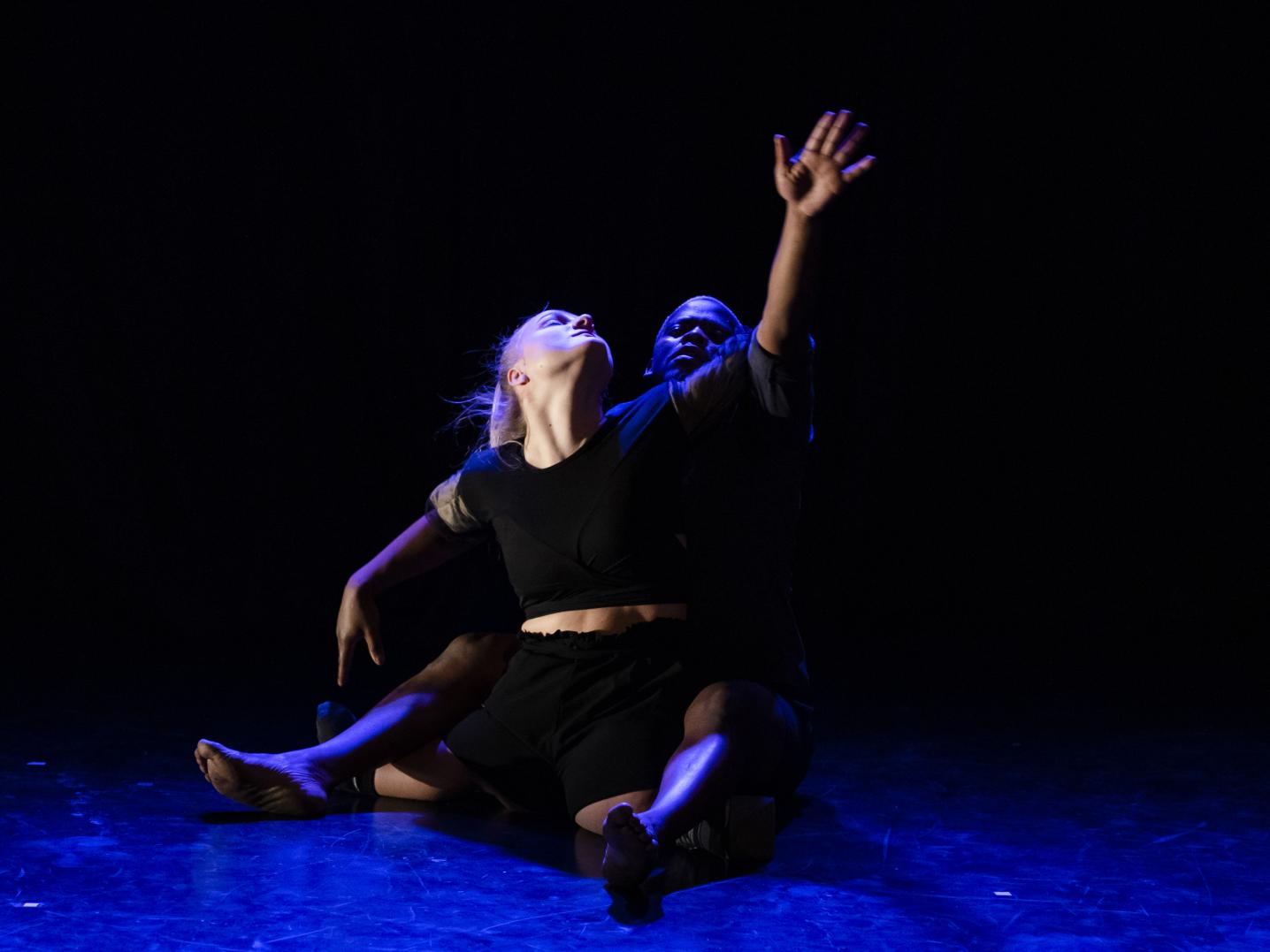 Two dancers are engaged in a performance, their bodies are entangled while their eyes are closed and their heads are raised above, suggesting a quite emotional moment in the performance. 