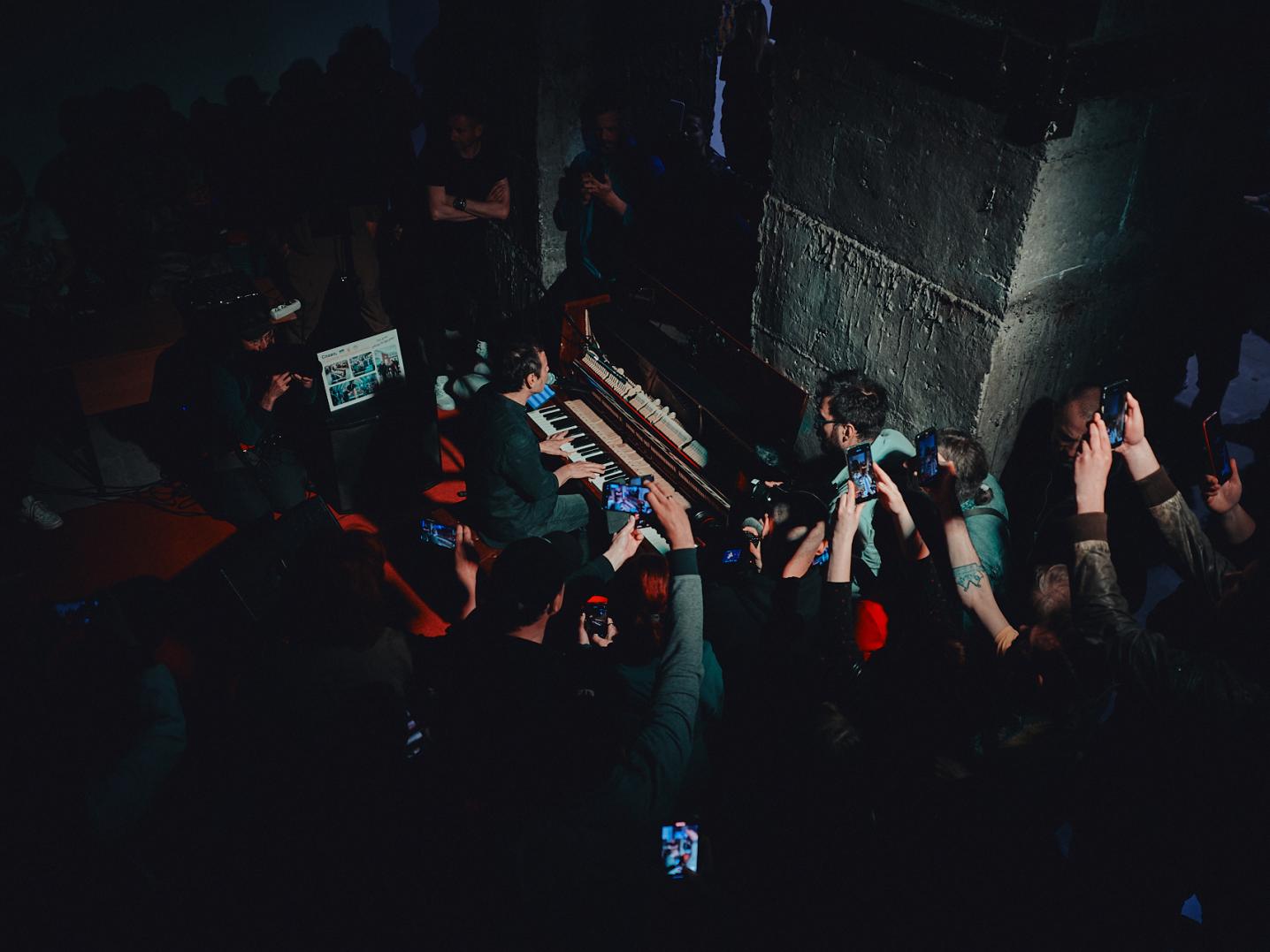 A pianist playing on stage surrounded by enthusiastic audience recording to performance