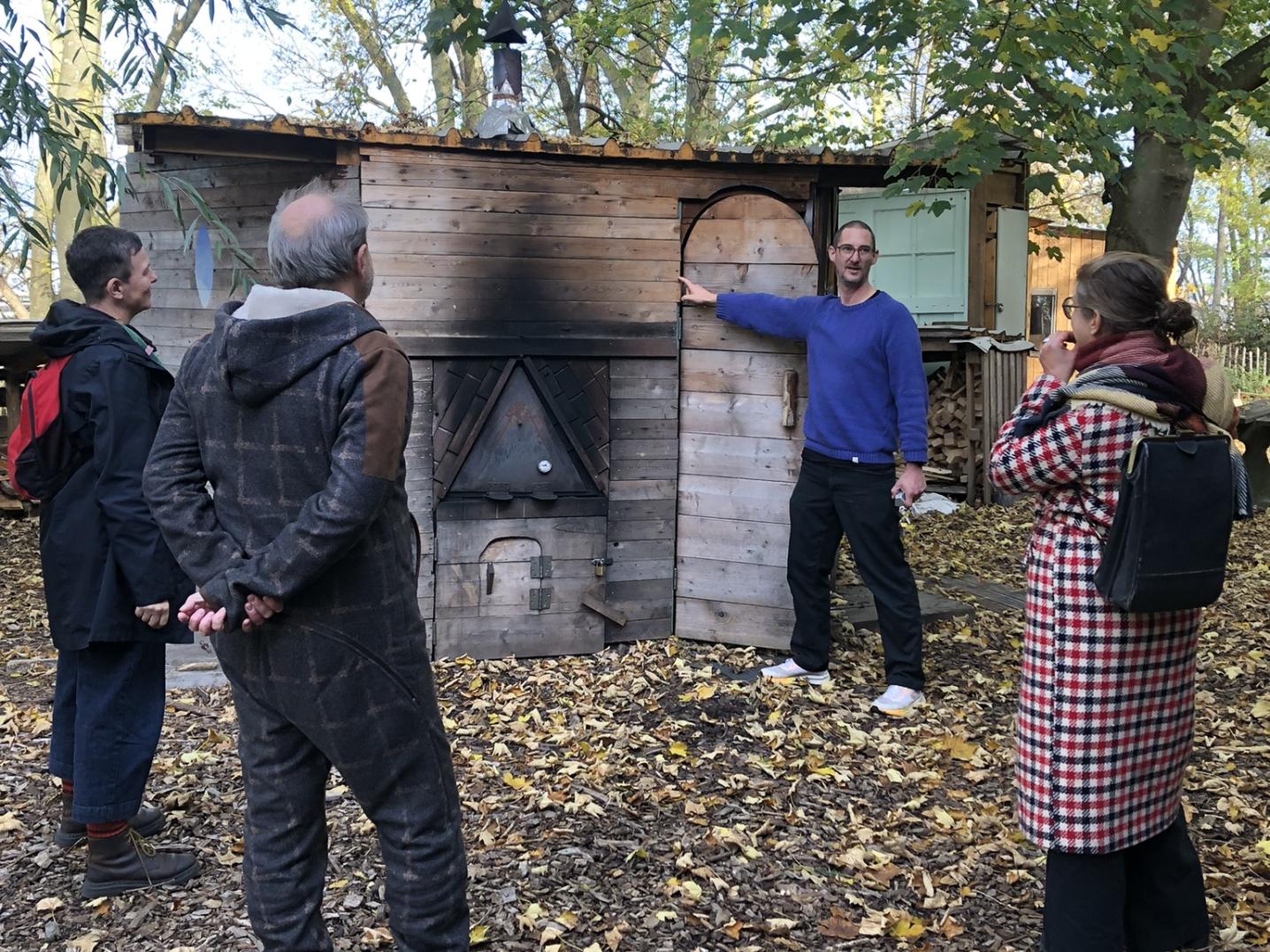People standing around and looking at a wooden sauna and pizza oven, created by an artist on the island Brienenoord in Rotterdam.