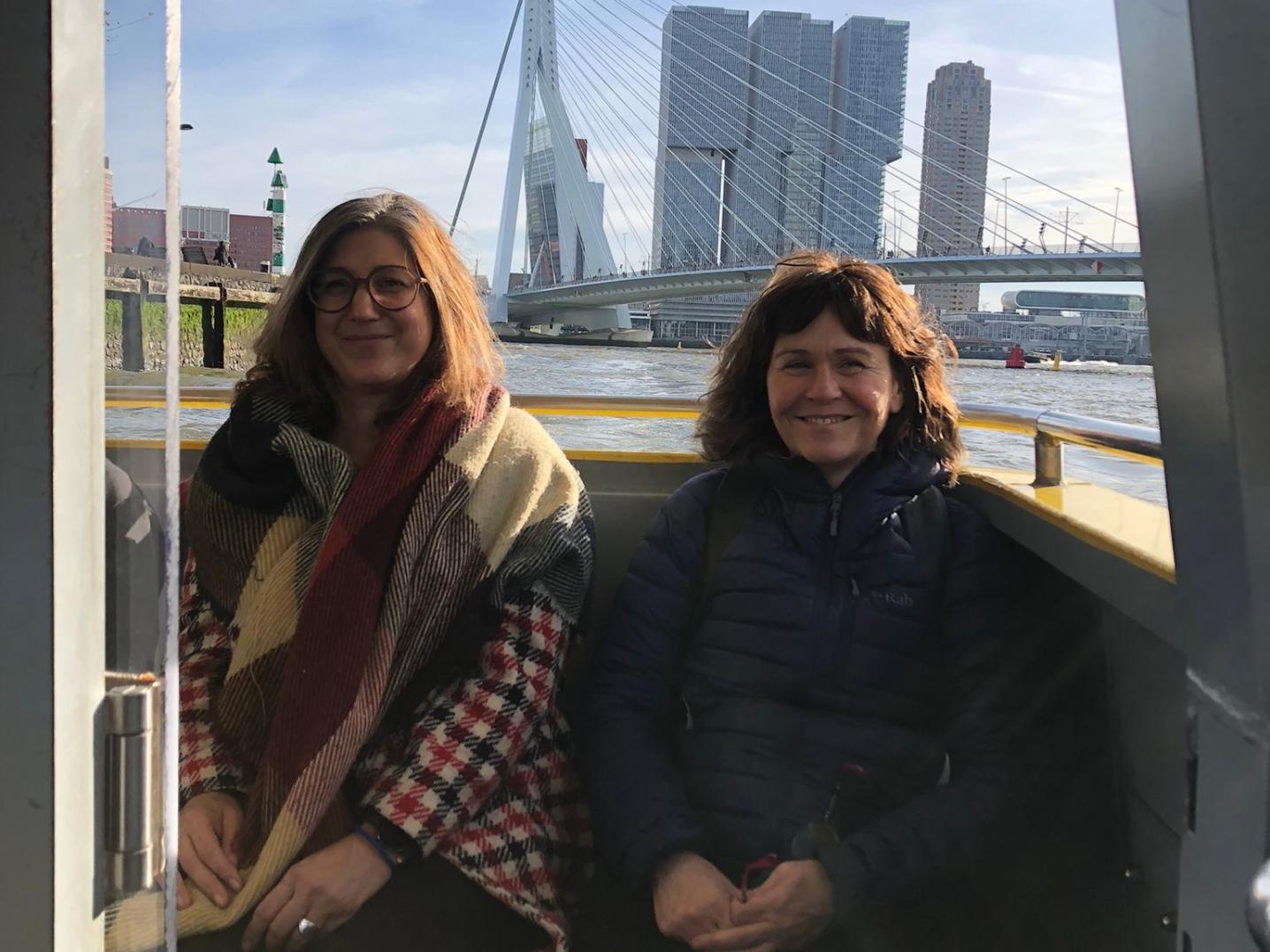 Two women in front of rotterdam landmark in boat on river