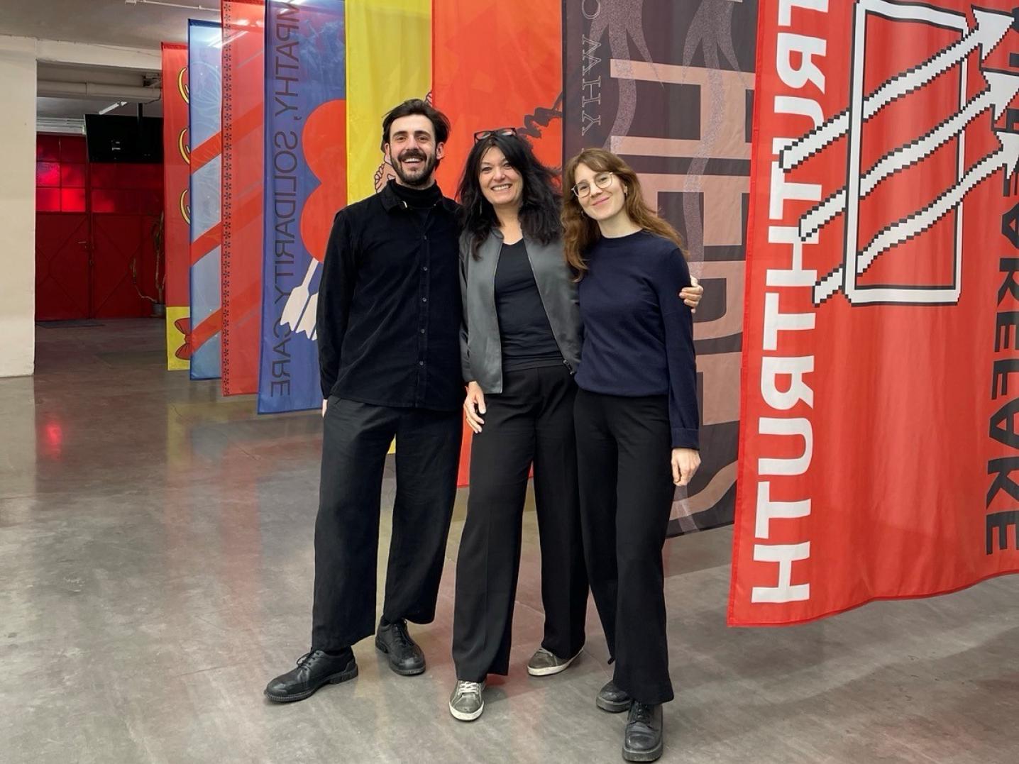 Three people standing in front of colorful, hanging fabric in an art exhibition hall.