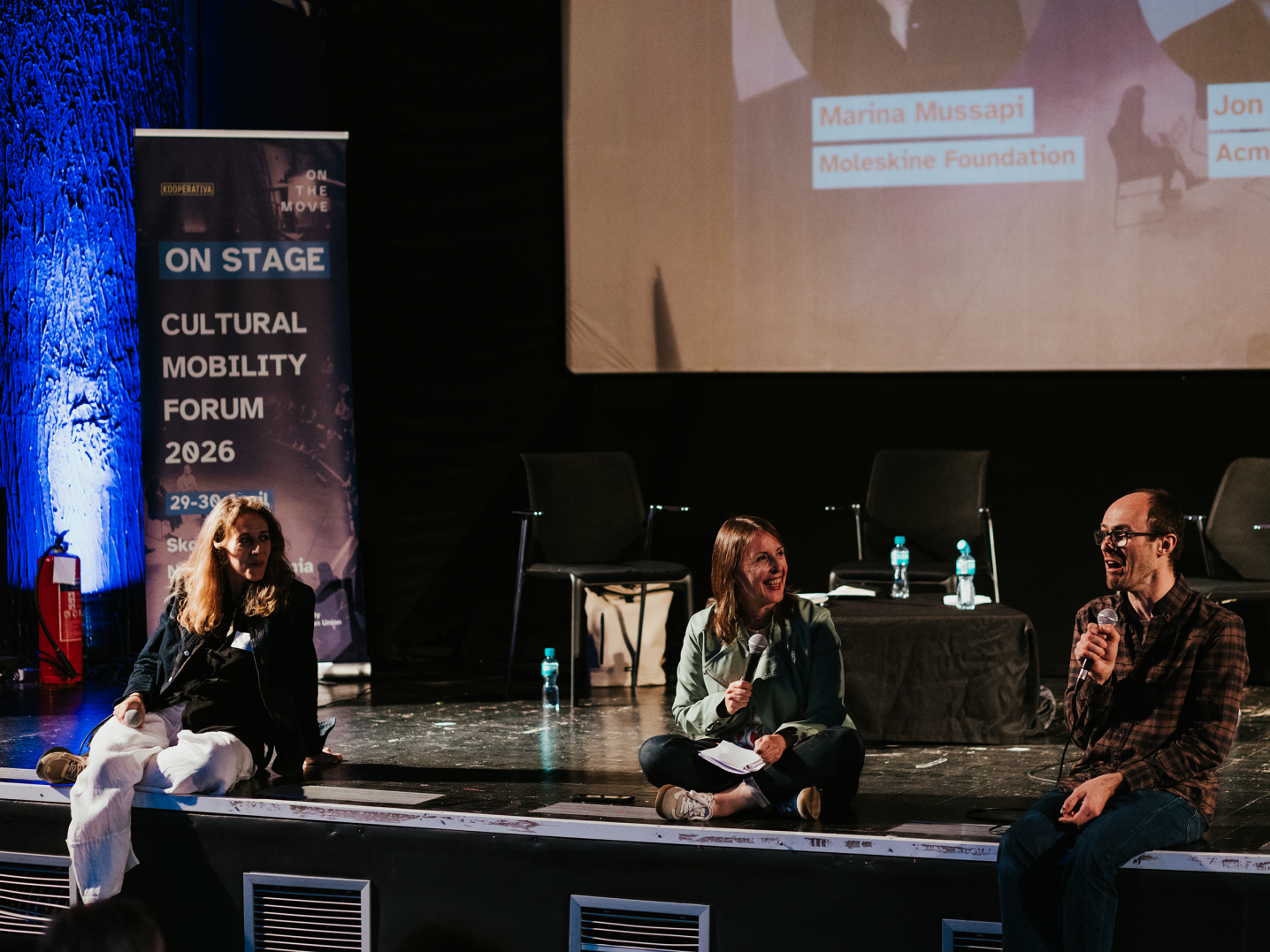 Three people sitting at the edge of the stage, having a panel talk