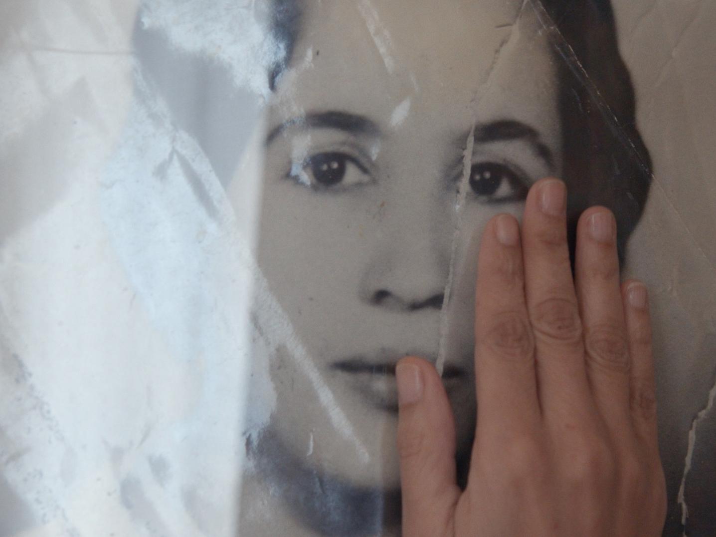A hand brushes over an image of a woman. Still from A Way Home.