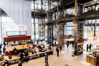 A group of people walking through a large industrial style hall with large windows