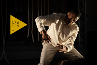 A black man making dance moves on a dark stage