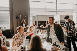 a group of people sitting at and standing around a table, two of them are ginving each other a high five