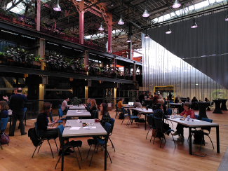 A group of people sitting around multiple tables in a large hall