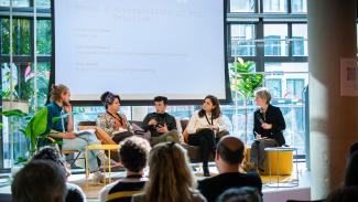 Four panelists are speaking about accessibility of art practice together with a moderator at a public event