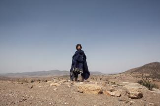 Woman wrapped in thick fabric standing in desert against blue horizon