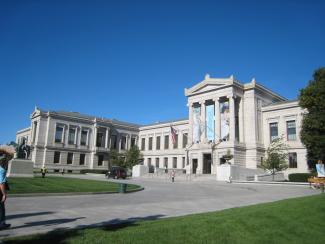 A large white building in neo classical style with a lawn in front and a clear sky