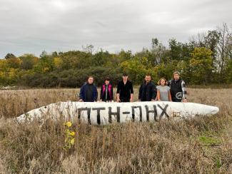six people standing in a field next to a fuel tank of a fighter jet in the Kharkiv region in Ukraine