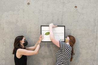 two women wearing facemasks holding a work a art against a grey wall in Cité Internationale des Arts, France