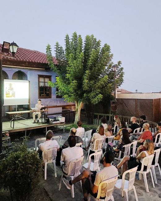 People sitting on chairs in a courtyard of Lucy Art Residency in Kavala, Greece watching a film