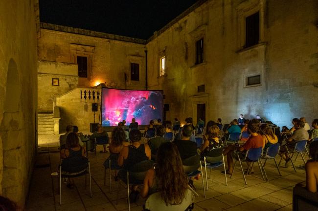 People sitting on chairs watching a film at night in the courtyard of KORA Contemporary Arts Center in Puglia, Italy