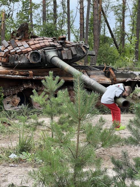 A boy playing on a burned-out Russian tank in the woods