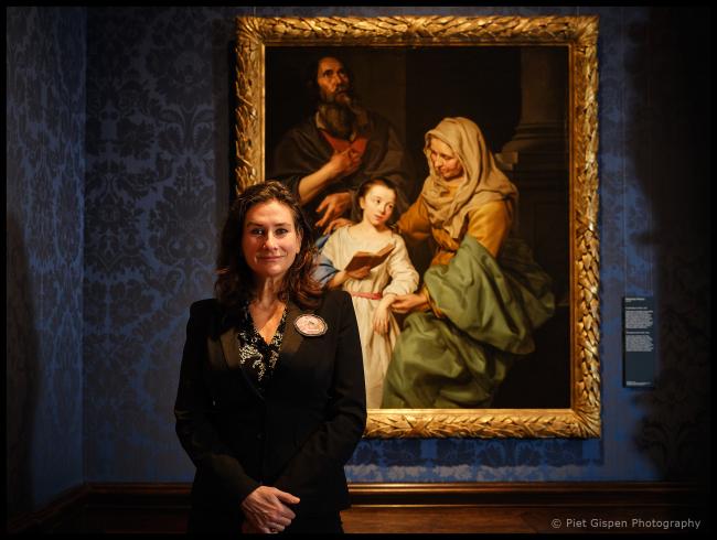 Martine Gosselink wearing a black suit standing crossed armed in front of a classical painting