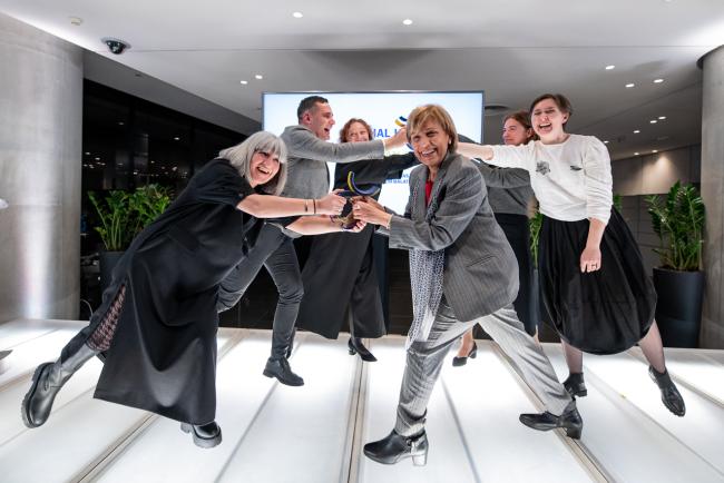 a group of people virtually handing over the European Cultural Capital title to another group of people, standing on a work of art