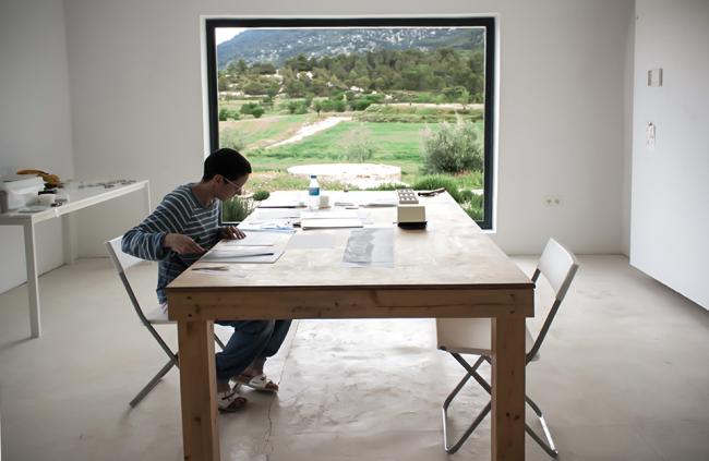 A person working while sitting at a table in a white room