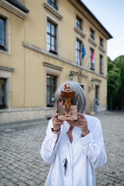 a woman standing in front of a building holding a statue that hides her face