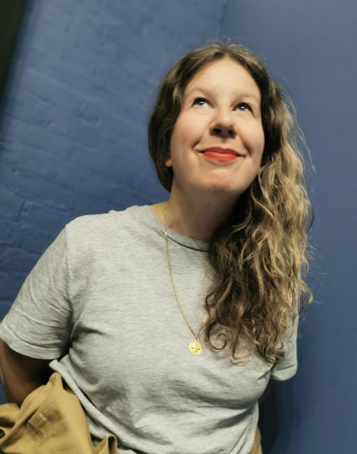 artist Maja Bekan looks up while posing in the corner of two dark blue walls