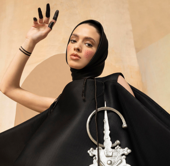 Fashion photo of a young woman dressed in black with long black nails posing in front of a wall
