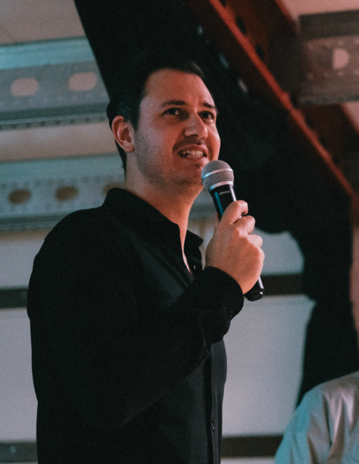 Tim Remmers holds a microfone while presenting in a black blouse