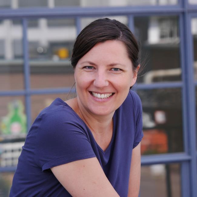 Woman wearing a dark blue shirt smiles in front of light blue colored window frames