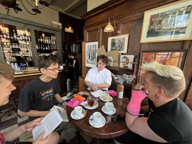 four people sitting around a table in a cafe talking and having coffee