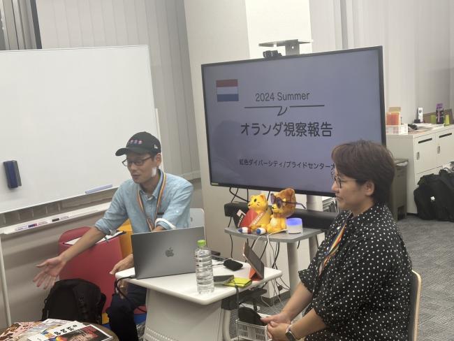 two people sitting in front of a beamer showing japanese text and a dutch flag