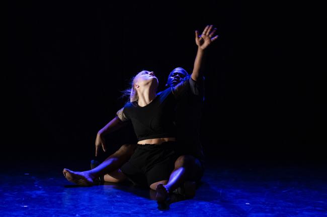 Two dancers are engaged in a performance, their bodies are entangled while their eyes are closed and their heads are raised above, suggesting a quite emotional moment in the performance. 