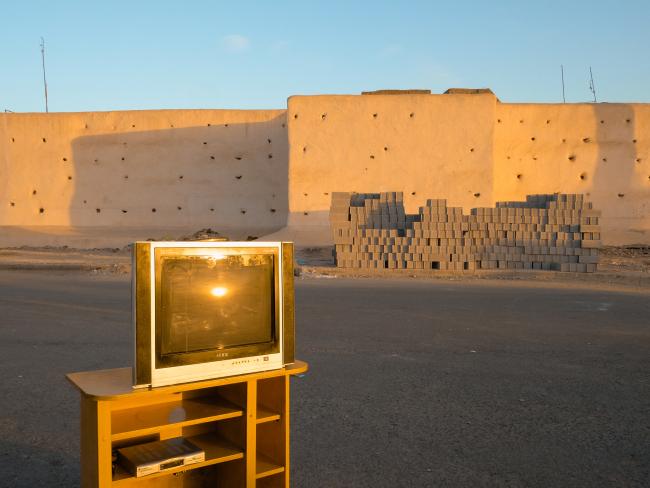 tv sitting on a tv cabinet on the side of the road next to a wall