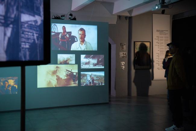 Dim exhibition space with a large screen showing multiple film clips. 