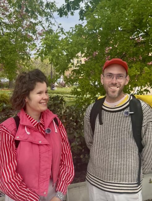 A young woman in pink coat with brown hair and a young man with glasses and a red cap. 