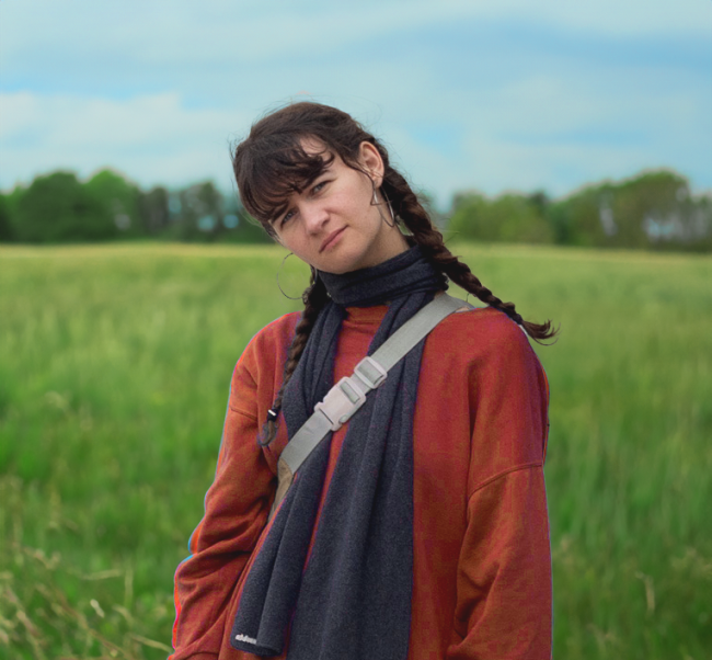 Girl standing in meadow with rusty-coloured jacket