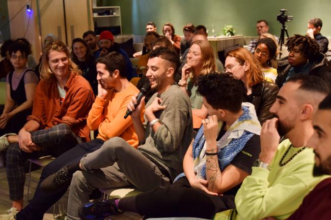 an audience in a room, people are laughing while one person is talking into a mic