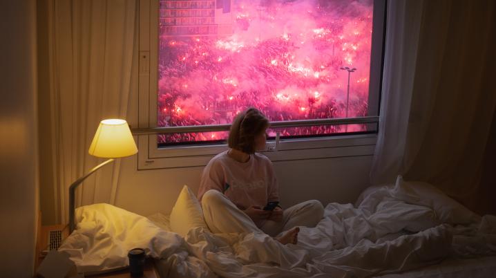 Woman sitting on bed in front of window with protest scene