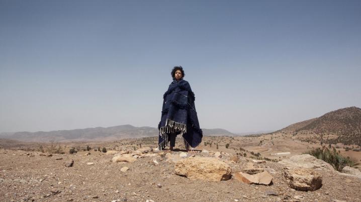 Woman wrapped in thick fabric standing in desert against blue horizon