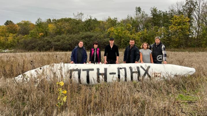 six people standing in a field next to a fuel tank of a fighter jet in the Kharkiv region in Ukraine